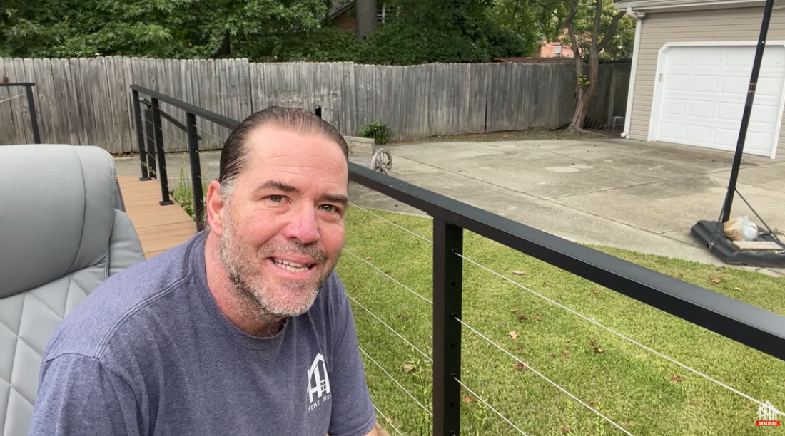 A man inspecting and adjusting a cable railing on his backyard deck.