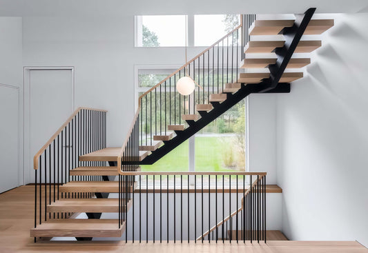 Floating wooden stairs ascend toward a sunlit window in a minimalist modern foyer.
